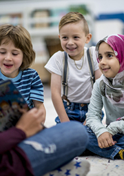 Young children on floor with teacher reading them a book.