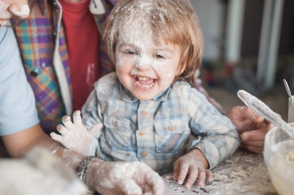 A toddler is having a blast playing with flour at the kitchen counter.