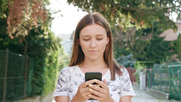 Teen girl walking outdoors as she looks at her smartphone.