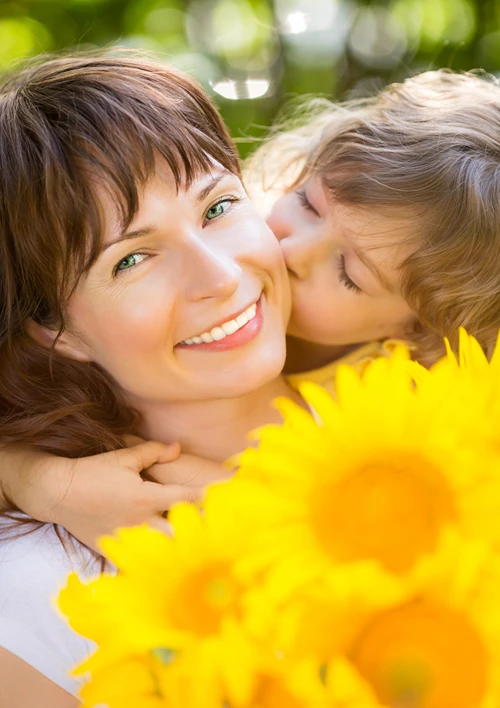 Mother holding flowers while being kissed by her child.