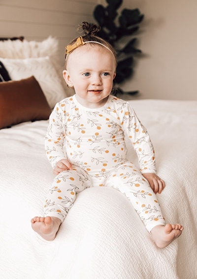 Smiling toddler sitting with feet hanging over corner of parent bed.