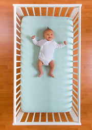 Overhead shot of cute baby lying on cot in crib.