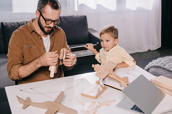 Dad and son putting together a wooden plane kit on coffee table in living room.