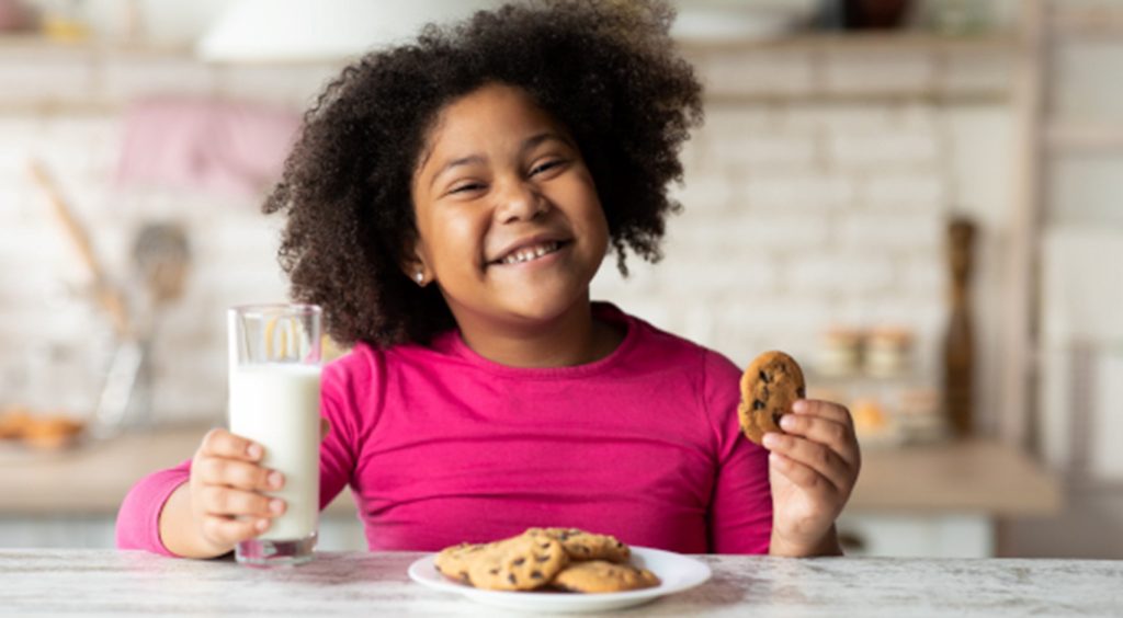 Joyful little girl eating cookies and milk.