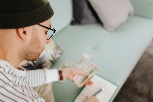 Man counting money while writing on note pad.