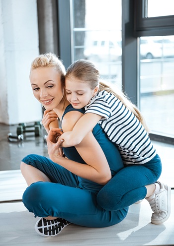 Daughter embraces mom from behind as she works out at home.