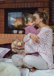 Mom holding and kissing her toddler in living room.