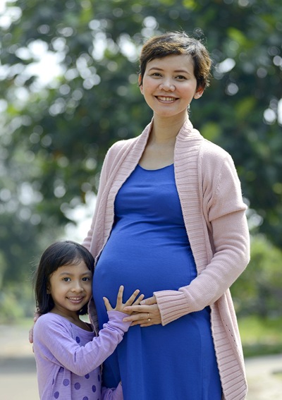 Pregnant mom posing with a little girl who is holding her hand on mom's tummy.