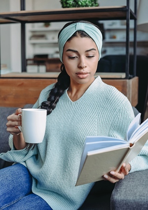 African American woman with coffee in one hand and a book in the other.