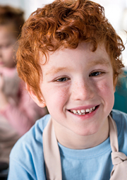 Boy wearing cooking apron smiling with sister in the background.