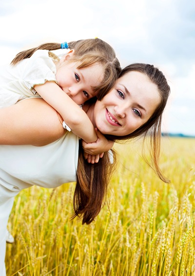 Daughter on mom's back standing in a wheat field.