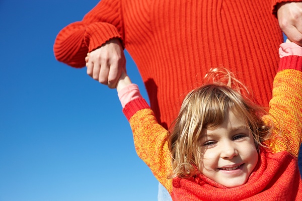 Girl happily hanging with both arms from her mother's tight grip.