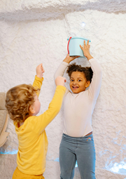 Girl holding small bucket over her head as if playing keep away from a younger child.