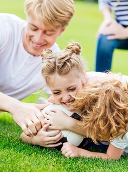 Girl laughing while holding soccer ball tightly on the ground.