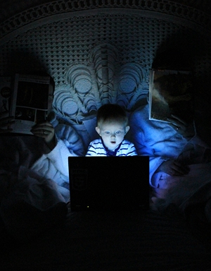 A wide-eyed child browsing the internet in the dark.