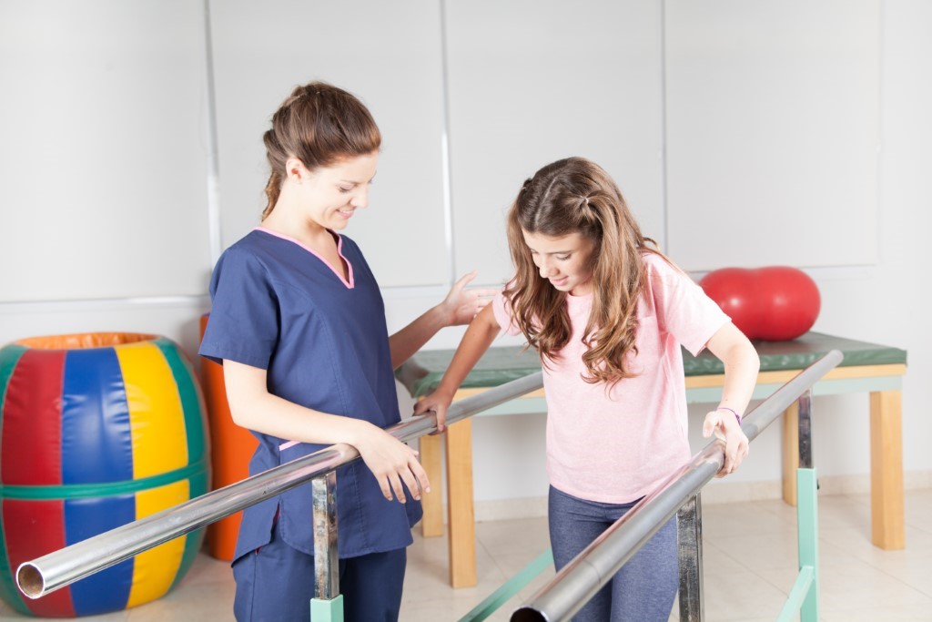 Physiotherapist working with injured girl on walking rails.