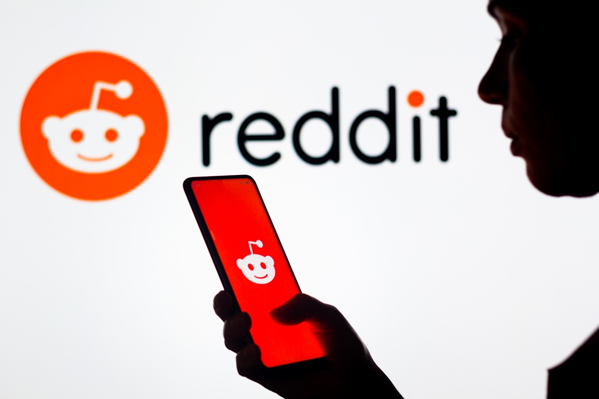 Silhouette of man viewing Reddit on his smartphone (with Reddit name and logo above)