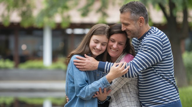 Teen daughter smiling and hugging parents.