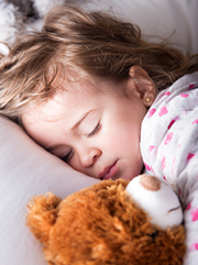 Girl Toddler holding teddy bear while selling soundly.