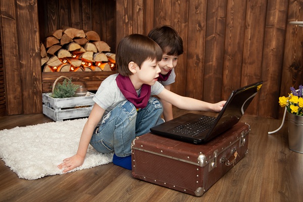 Two boys playing on laptop that is sitting on an old suitcase on the floor.