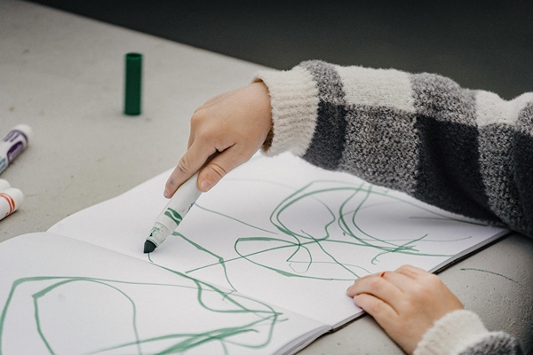 Young child drawing in coloring book with a green marker.