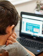 Boy resting chin in his hands looking at laptop screen.