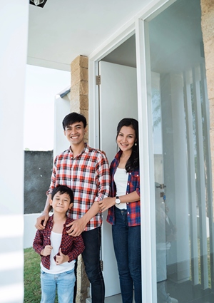 A Family is standing and smiling in open patios doors of their home.