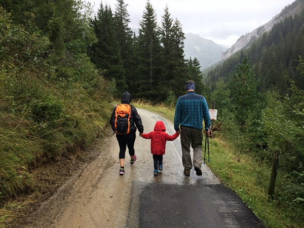 Boy holding hands between two adults walking on a dirt path in the wilderness.