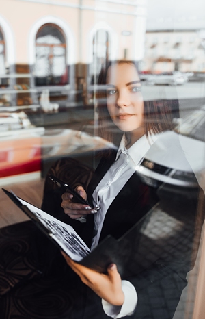 Serious looking professionally dressed woman holding binder with documents, superimposed over reflection of busy street.