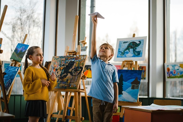 Girl and boy in room surrounded by paintings on various sized easels.