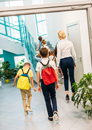 Kids with backpacks walking in school hallway with teacher.