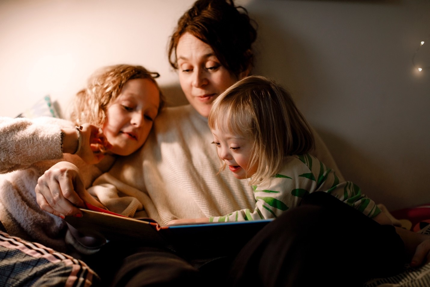 Mom reading book to two girls in bed.