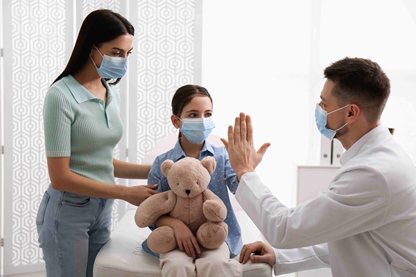 Young girl holds teddy bear and high fives her Pediatrician.