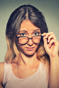 Skeptical woman pulling her glasses down as looking at something with doubt.