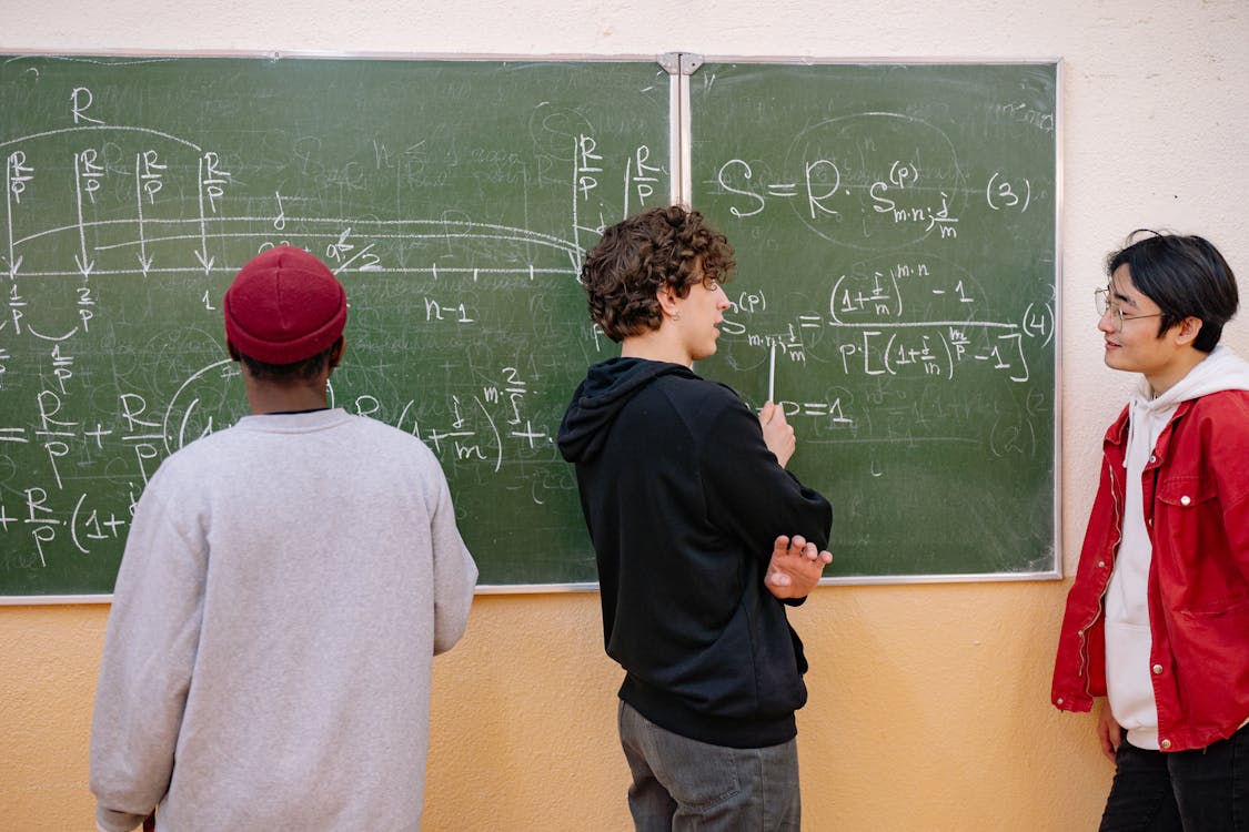 Three teen boys doing math on blackboard at school at school.