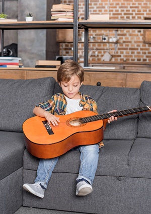 Young boy holding classical guitar on his lap and trying to play it.