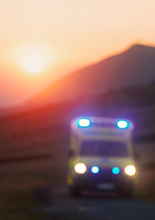 Ambulance with flashing lights driving as sun sets in background.