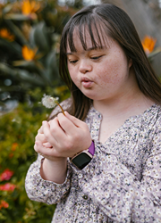 Autistic girl blowing the petals of a dandelion.