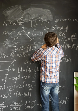 Boy doing complicated math on blackboard with back to the classroom.