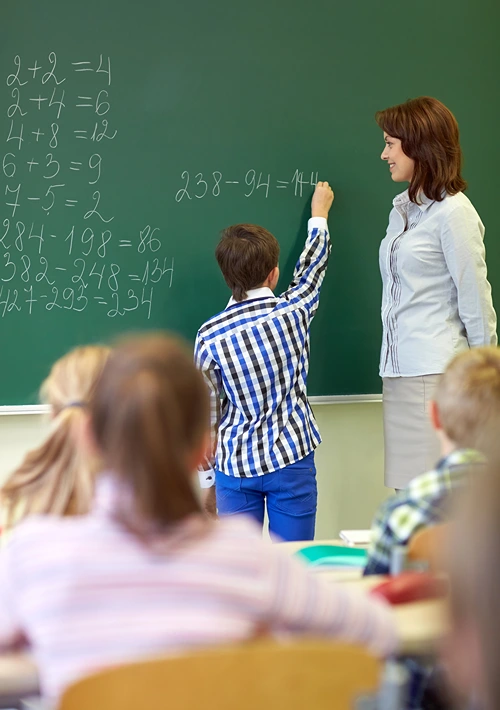 Boy doing math on blackboard in front of class.