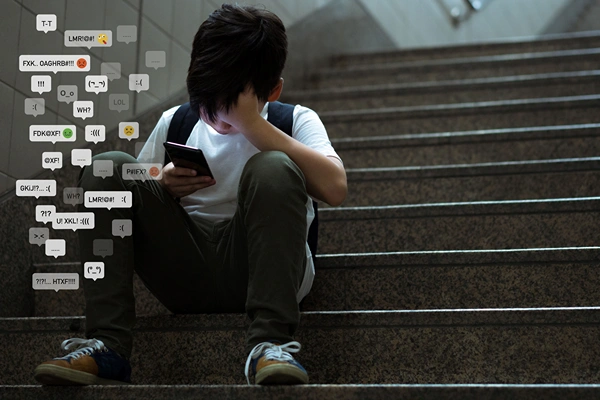 Boy sitting on school steps with head in hands as comments pop up from his phone.