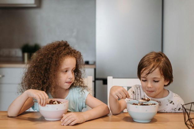 Brother and sister eating out of big white bowls at the kitchen table, 