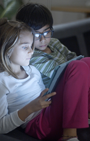 Brother and Sister watch tablet with glow of screen on their faces.