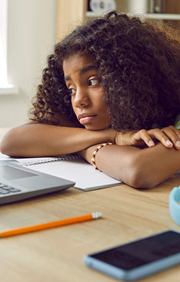 Depressed looking girl resting her head on arms on a desk.