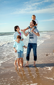 Mom, dad, and two kids wading in the Water on a sandy beach.