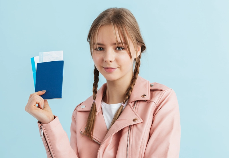 Teen girl with slight smile holding up passport in her hand.