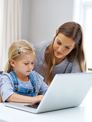 Mother stands over daughter seated at lap top.