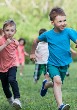 Boys running in front of group of kids on green grass.