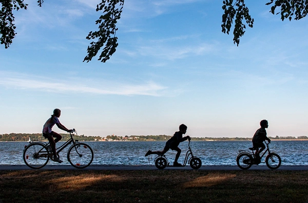 Kids riding bikes and scooters along lake shore.