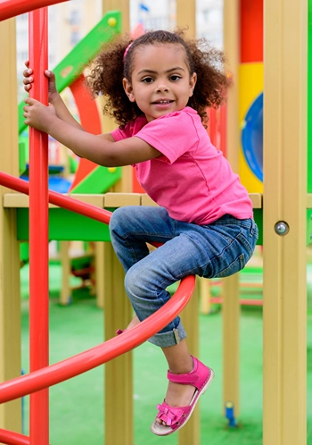 Smiling little girl climbing on public playground equipment.